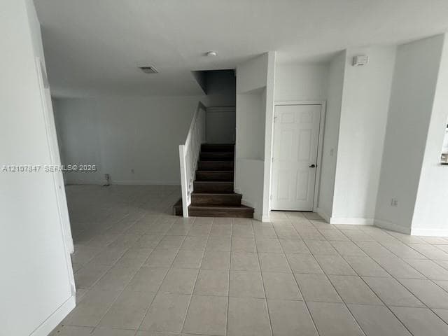 Neutral-toned ceramic tile flooring, staircase with wood-finish treads, white handrail, and built-in recessed wall niche