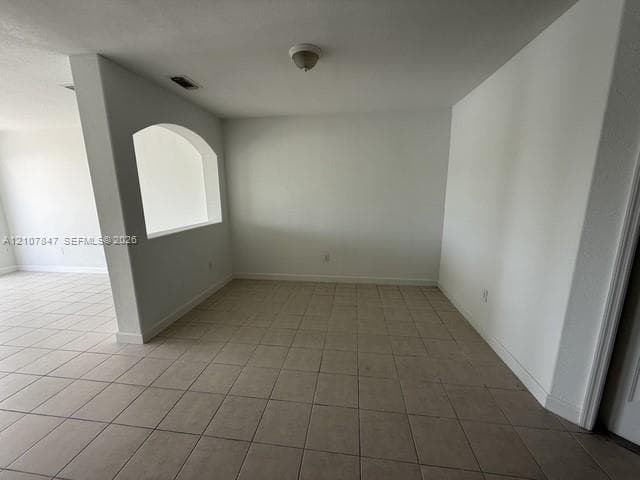 Interior space featuring neutral tile flooring, smooth white walls, a structural arched wall cutout, and a ceiling-mounted light fixture