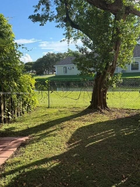 Backyard featuring a paved patio, expansive lawn, mature tree, chain-link fencing, and water frontage