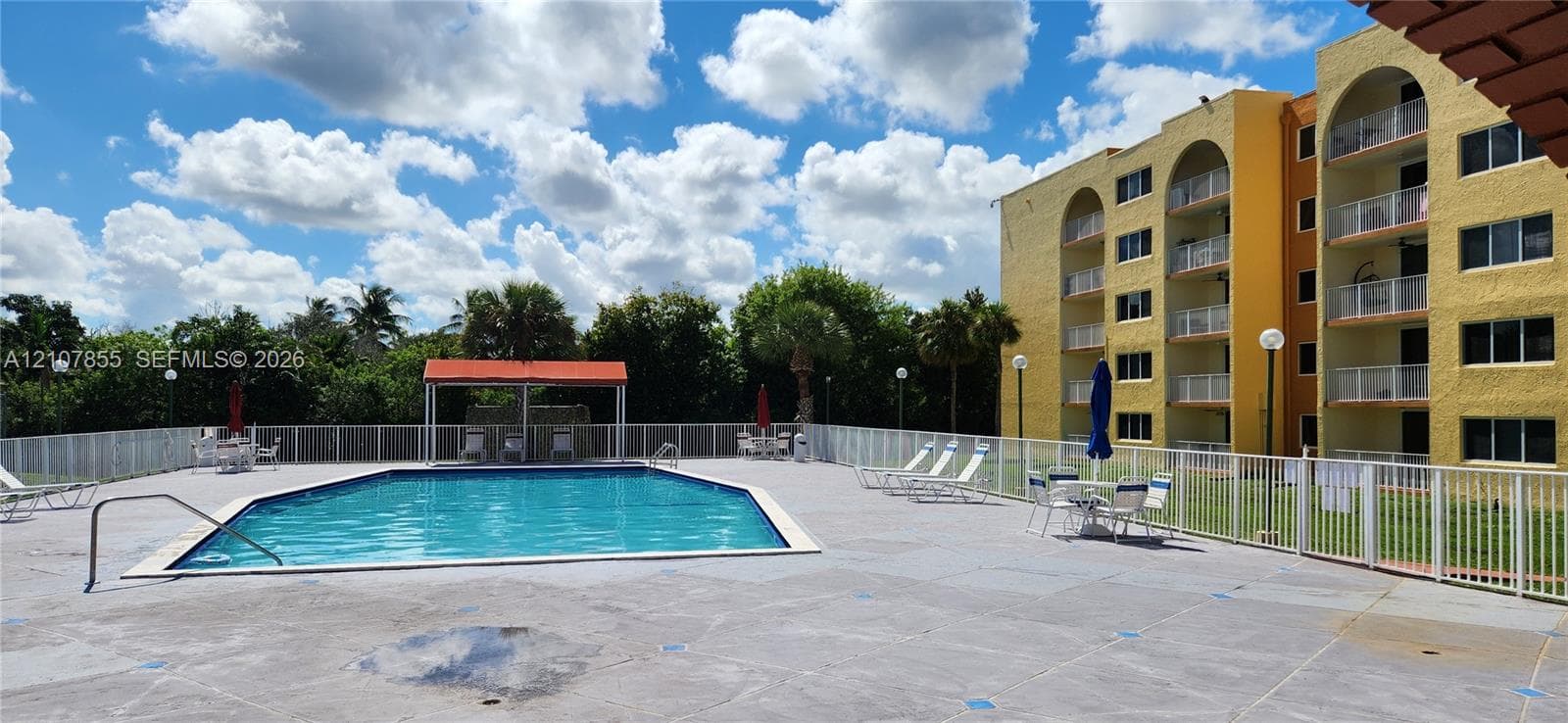 Outdoor swimming pool with a concrete deck, metal perimeter fencing, and a covered pavilion structure
