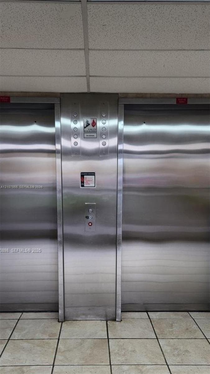 Dual stainless steel elevators featuring brushed metal finishes, center call panel, and light-toned tile flooring