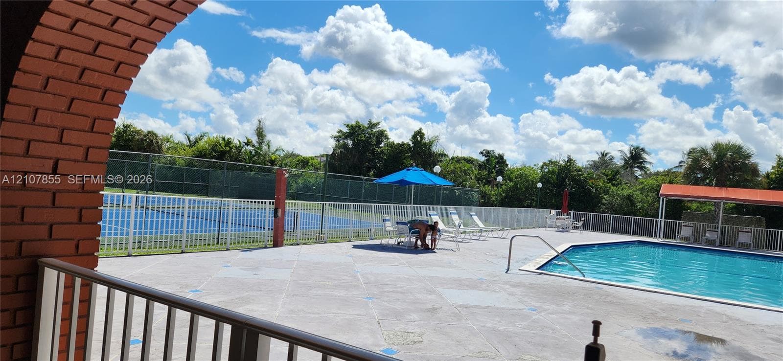 Outdoor recreation area featuring a swimming pool, tennis court, brick-arched exterior detail, and perimeter fencing