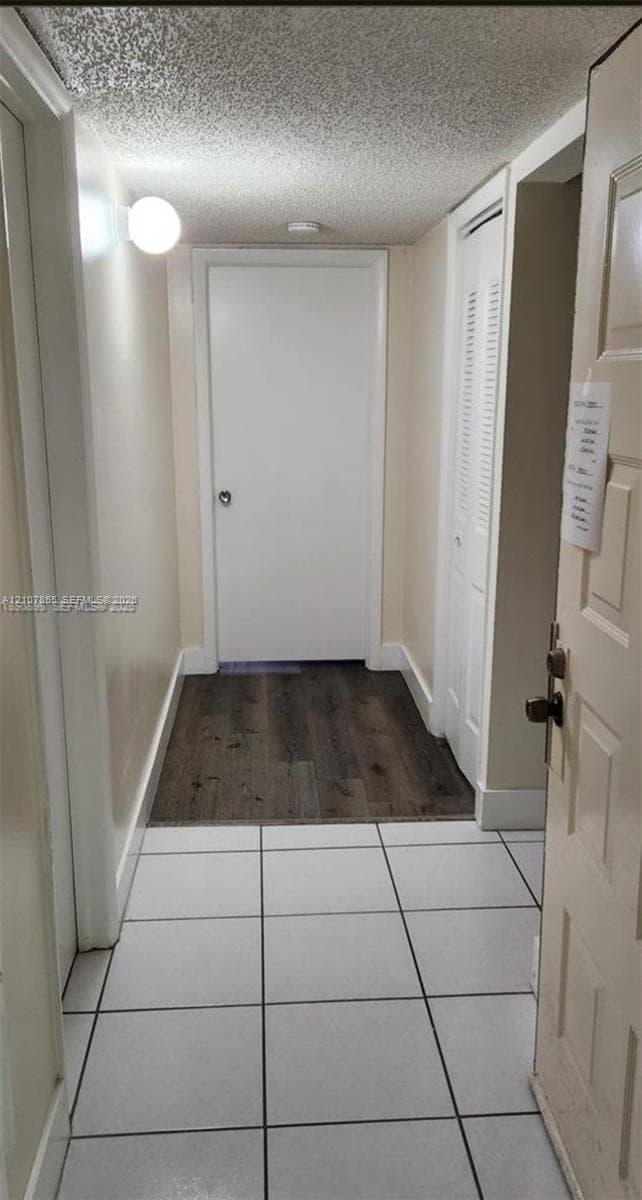 Interior hallway featuring large-format ceramic tile flooring, wood-finish flooring accents, and a paneled closet door with louvered venting