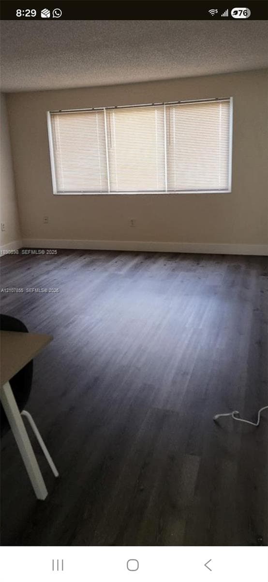 Spacious room featuring wood-finish flooring, neutral wall tones, and a large three-panel window