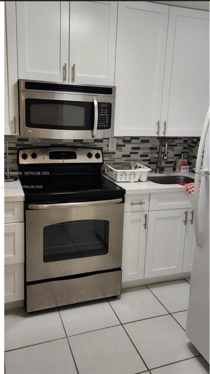 Kitchen featuring white shaker-style cabinetry, stainless steel appliances, a stone-surface countertop, tile backsplash, and a sink with a gooseneck faucet