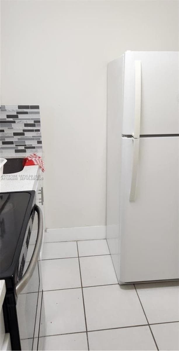 White top-freezer refrigerator, white ceramic tile flooring, and multi-tone mosaic tile backsplash