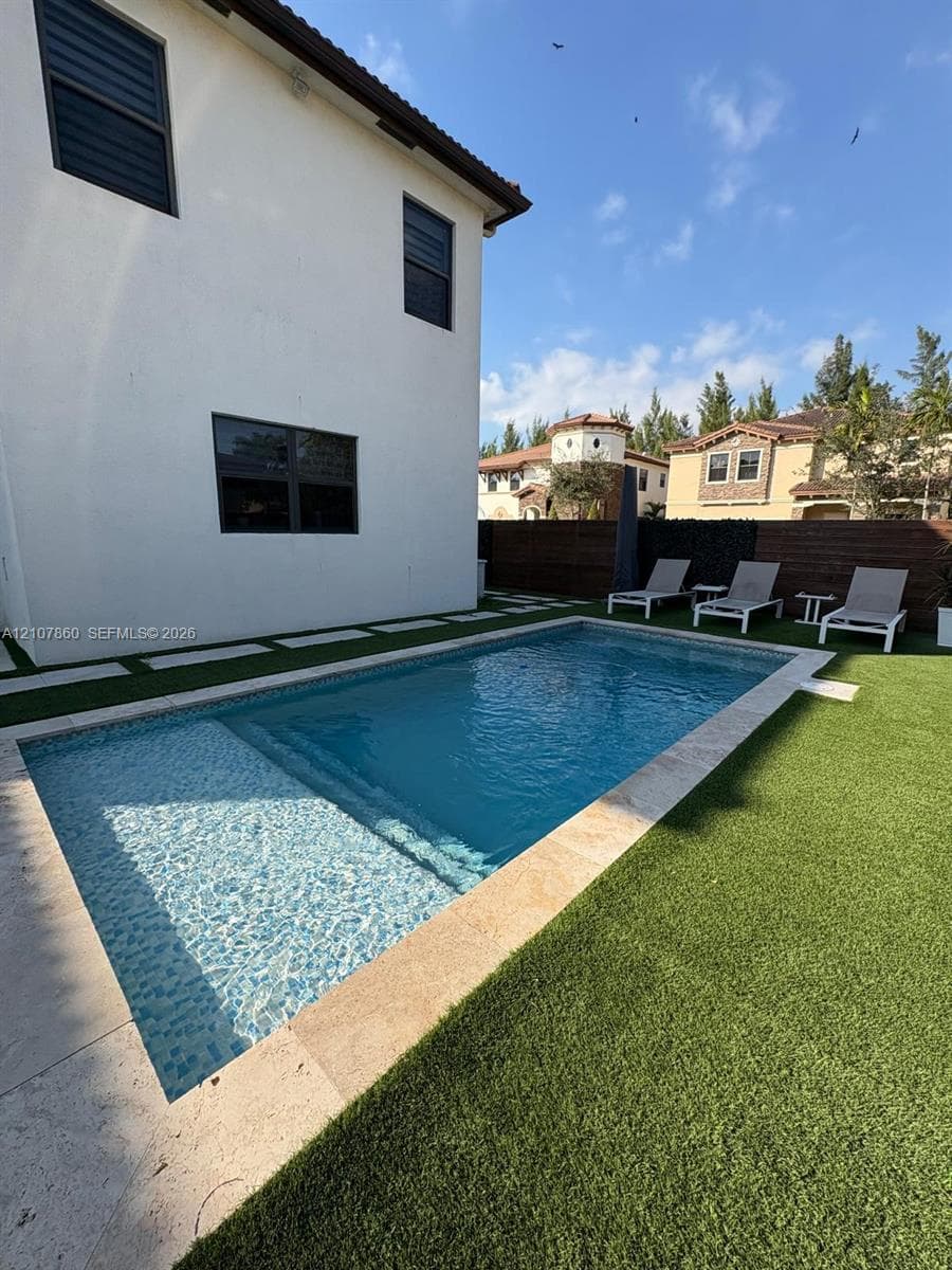 Rectangular swimming pool featuring a tanning ledge and natural stone coping, surrounded by synthetic turf and oversized concrete pavers, enclosed by a horizontal wood fence