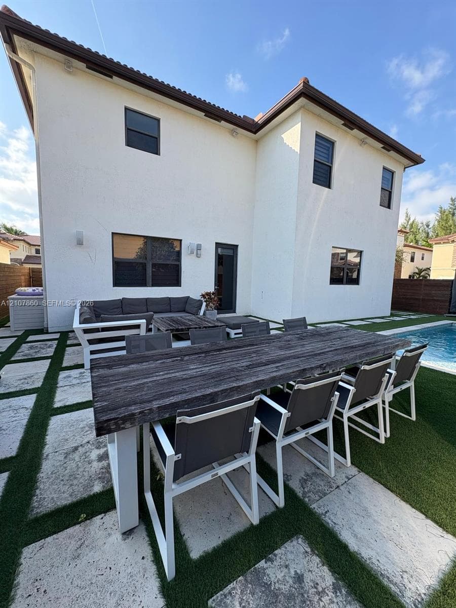 Stucco exterior with a multi-level roofline, swimming pool, and geometric paver patio with integrated synthetic turf