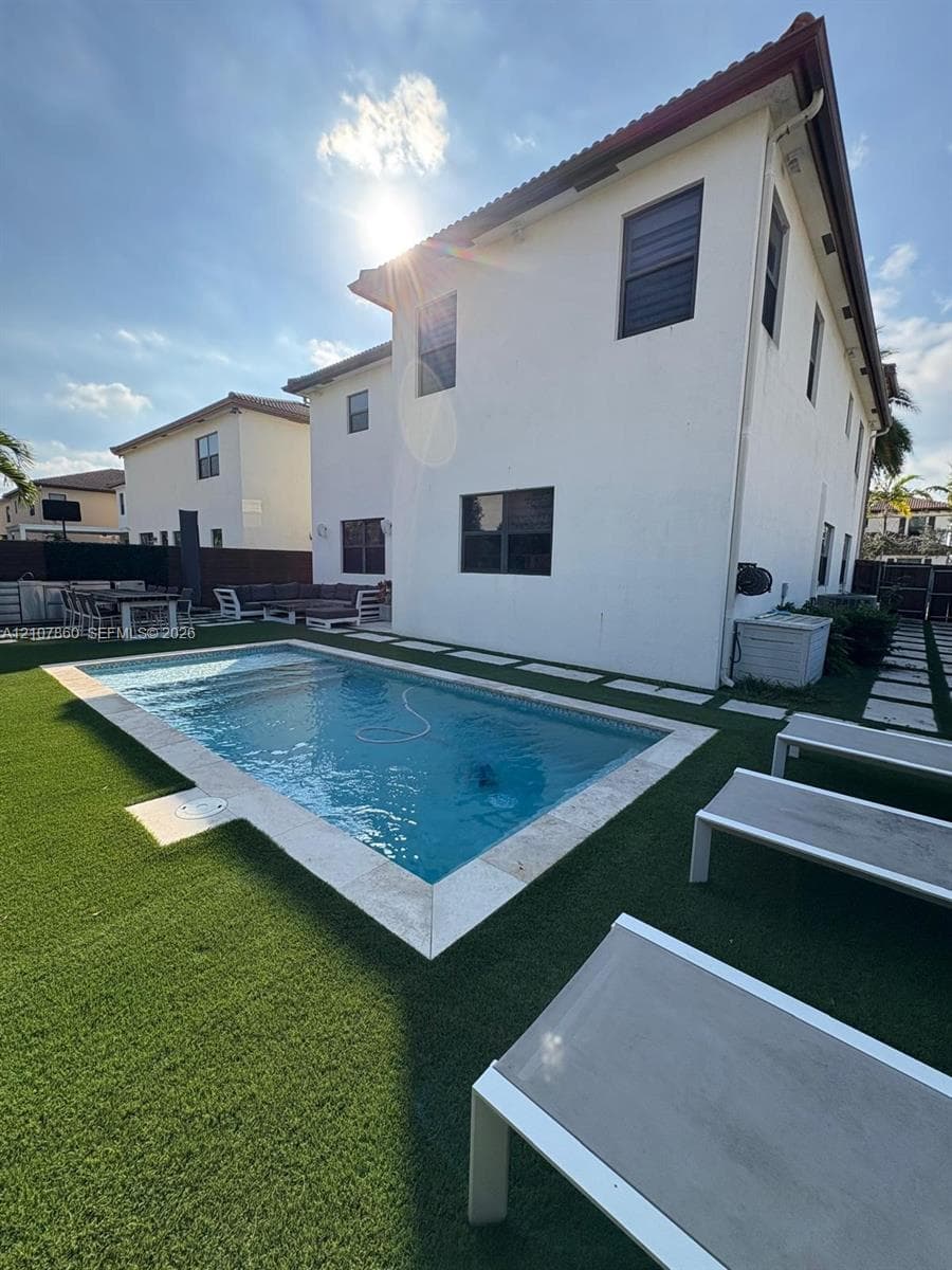 Rectangular swimming pool featuring stone coping, synthetic turf landscaping, and paved hardscaping