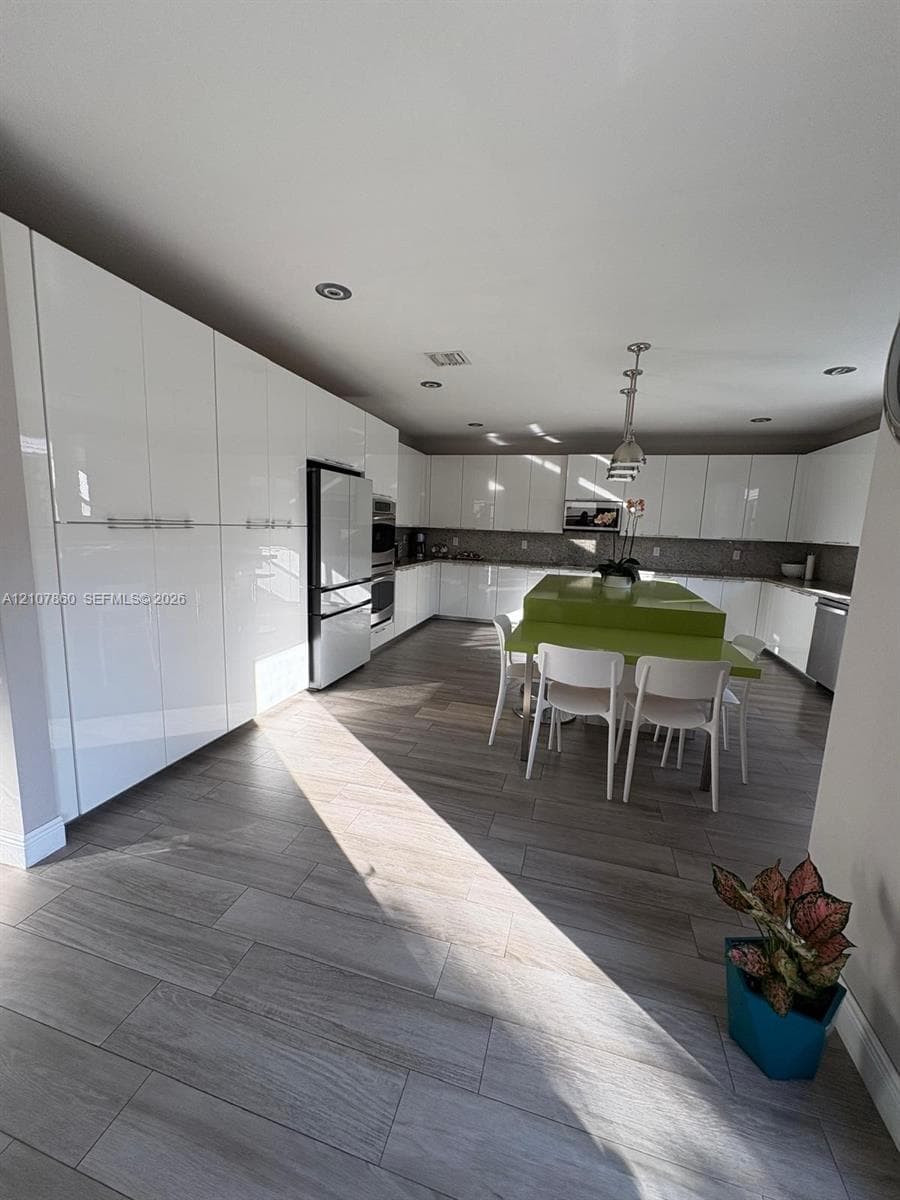 Kitchen featuring high-gloss white cabinetry, expansive stone-surface center island, wood-finish tile flooring, recessed ceiling lighting, and stainless steel built-in appliances