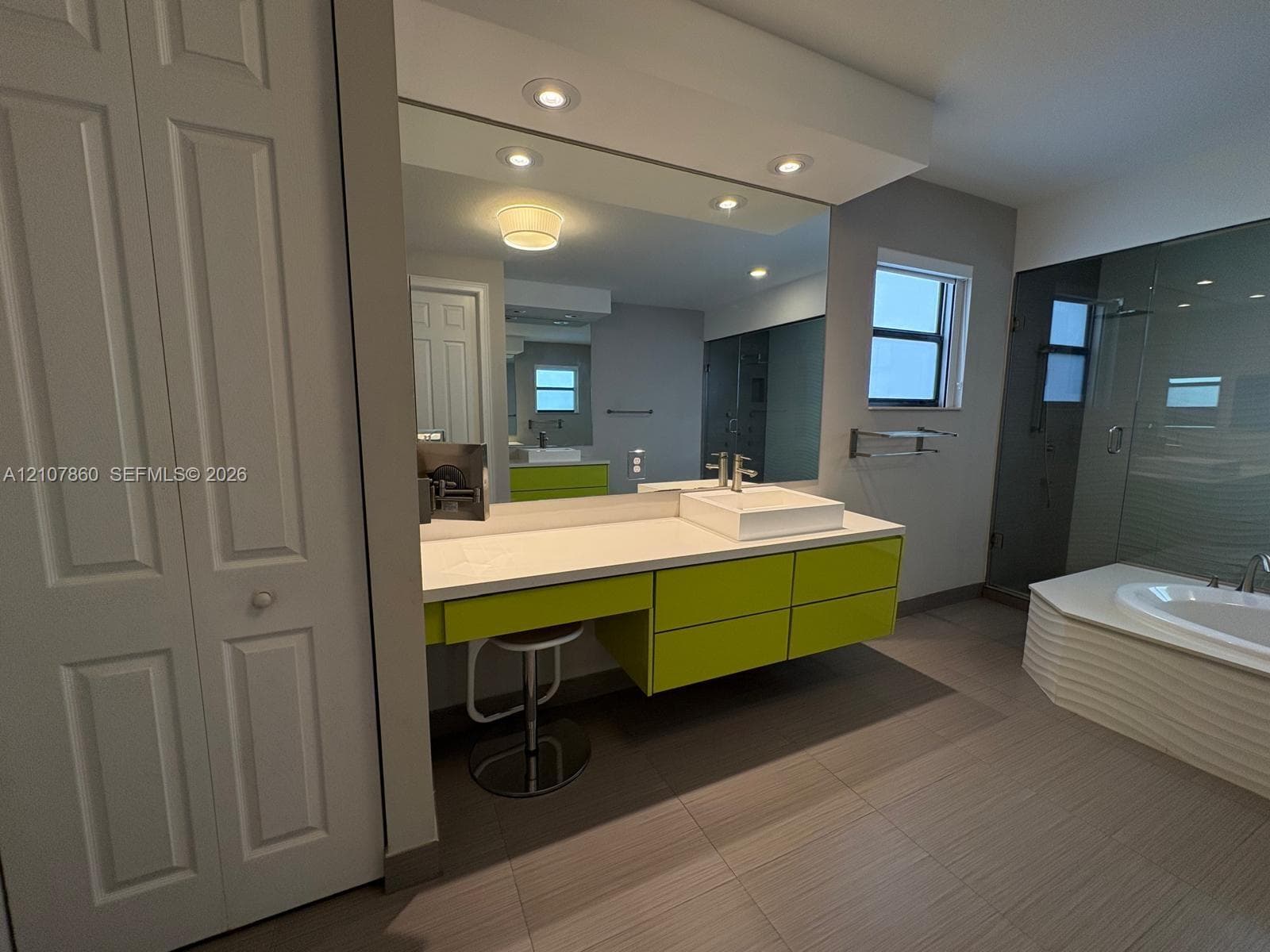 Floating vanity with a rectangular vessel sink and solid-surface countertop, full-width mirror, recessed lighting, tile flooring, and a glass-enclosed shower with a soaking tub