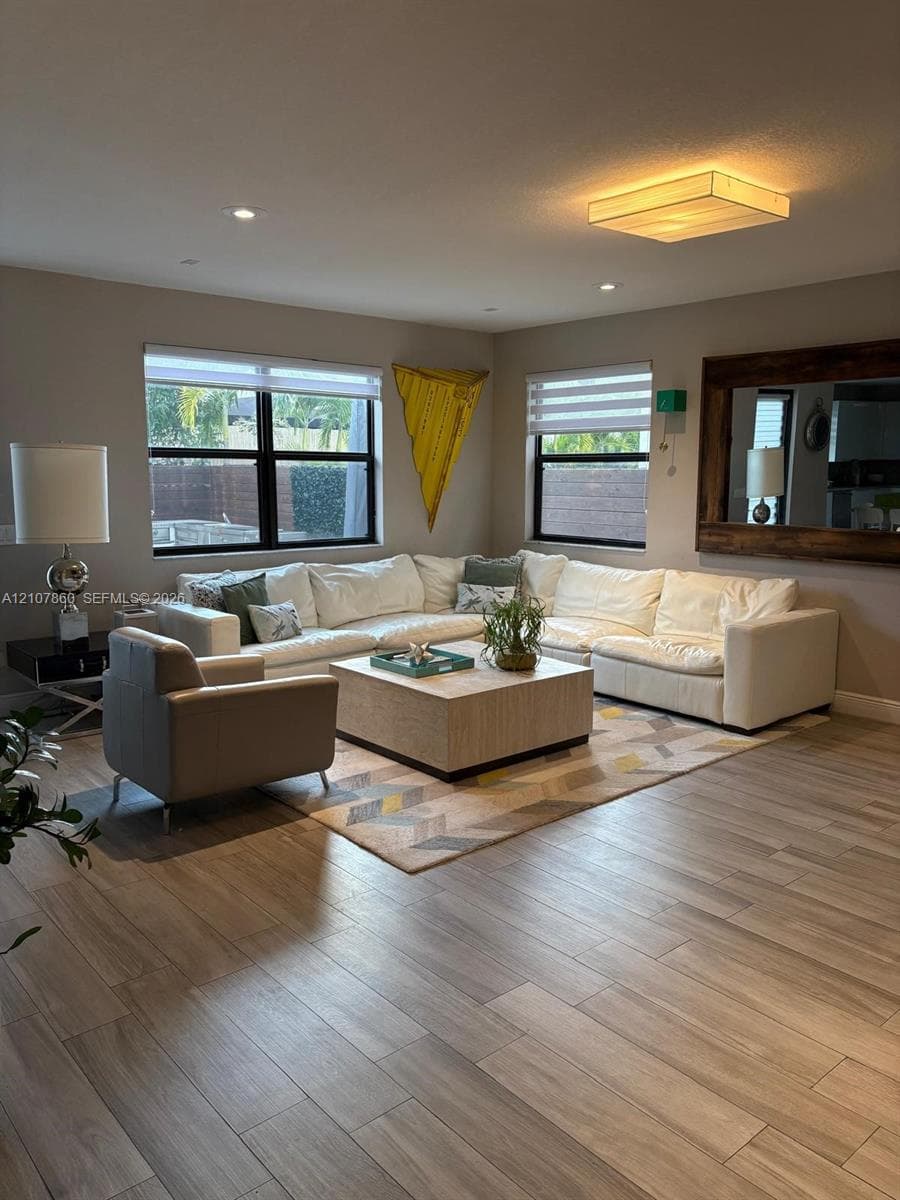 Living area featuring wood-finish flooring, dual windows with roller shades, recessed ceiling lighting, a flush-mount rectangular light fixture, and a large wall-mounted mirror with a rustic wood frame