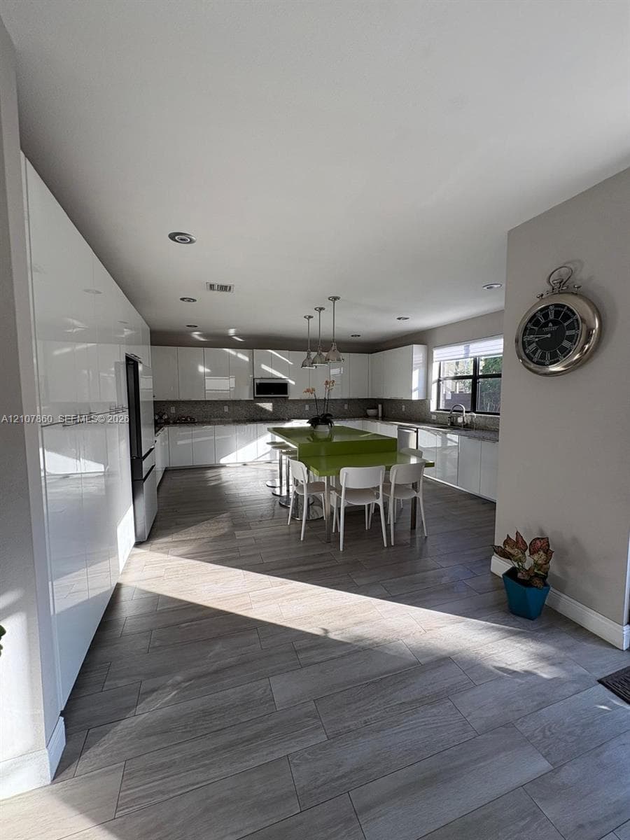 Kitchen featuring high-gloss white cabinetry, wood-finish flooring, a central island with a solid-surface countertop, recessed lighting, and stainless-steel built-in appliances