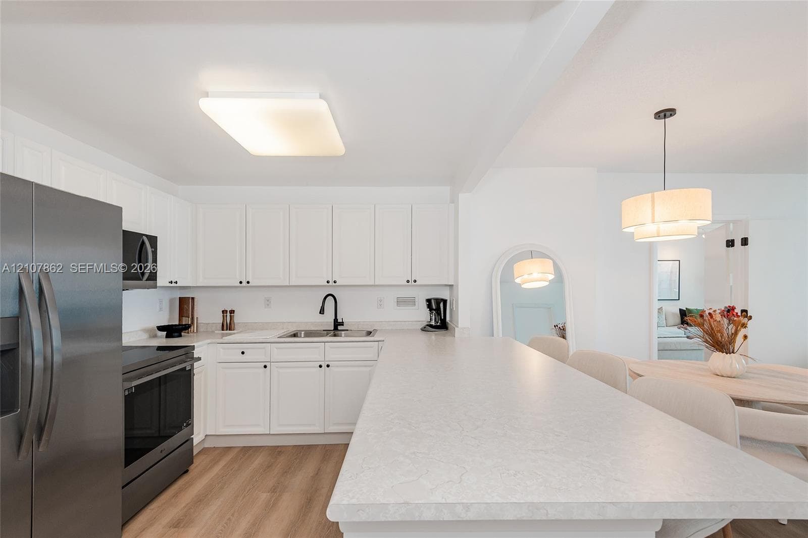 Kitchen featuring white shaker-style cabinetry, a stone-finish breakfast bar, wood-finish flooring, stainless steel appliances, and a matte black faucet