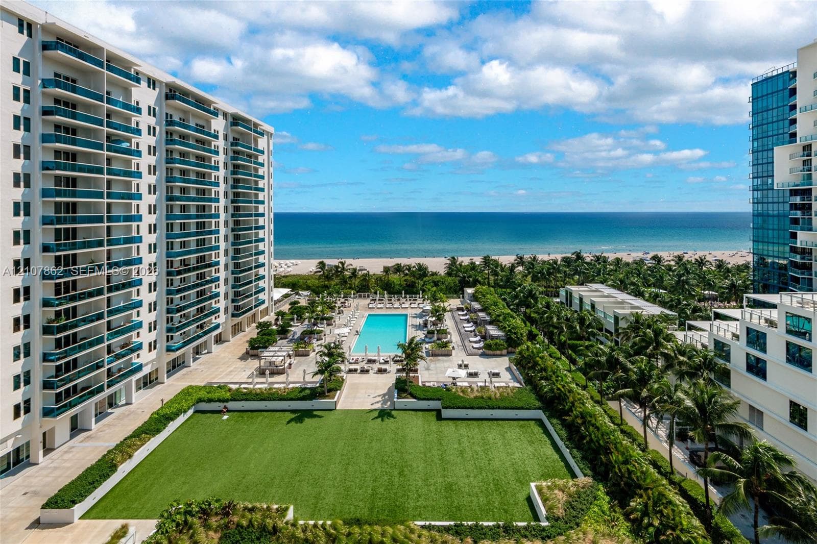 Expansive outdoor common area featuring a manicured lawn, paved pool deck, swimming pool, and direct oceanfront access