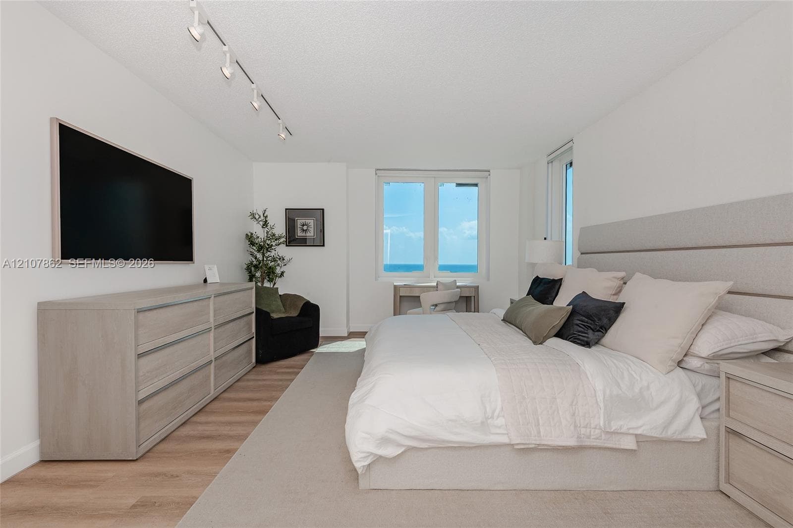 Room featuring wood-finish flooring, adjustable track lighting, and a large window with ocean scenery