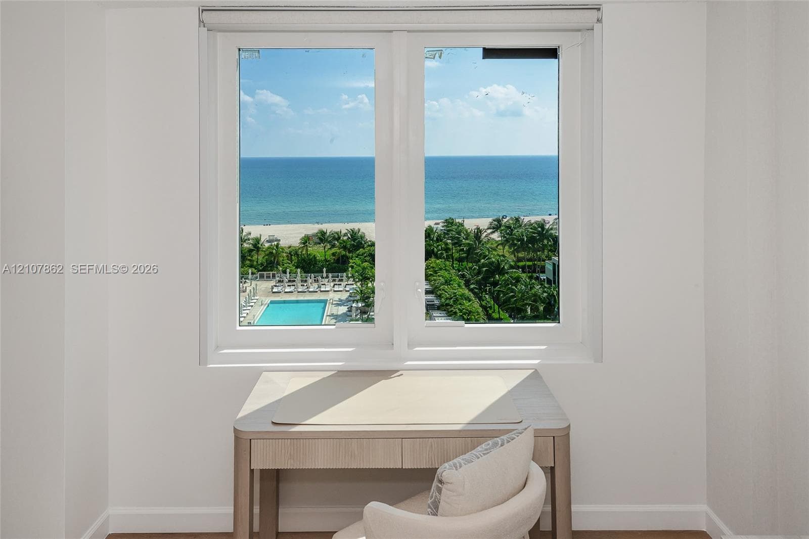 Double-paned white-framed window overlooking the coastline, sandy beach, and swimming pool