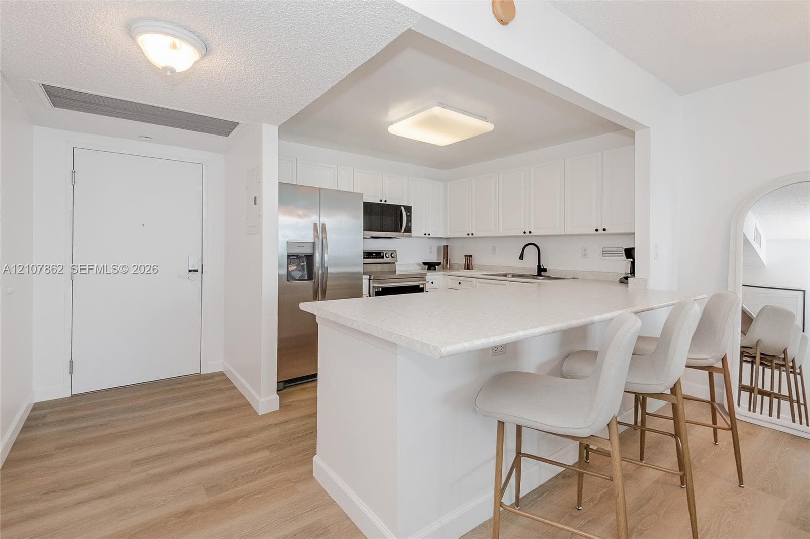 Kitchen featuring white cabinetry, wood-finish flooring, stainless steel appliances, and a solid-surface breakfast bar