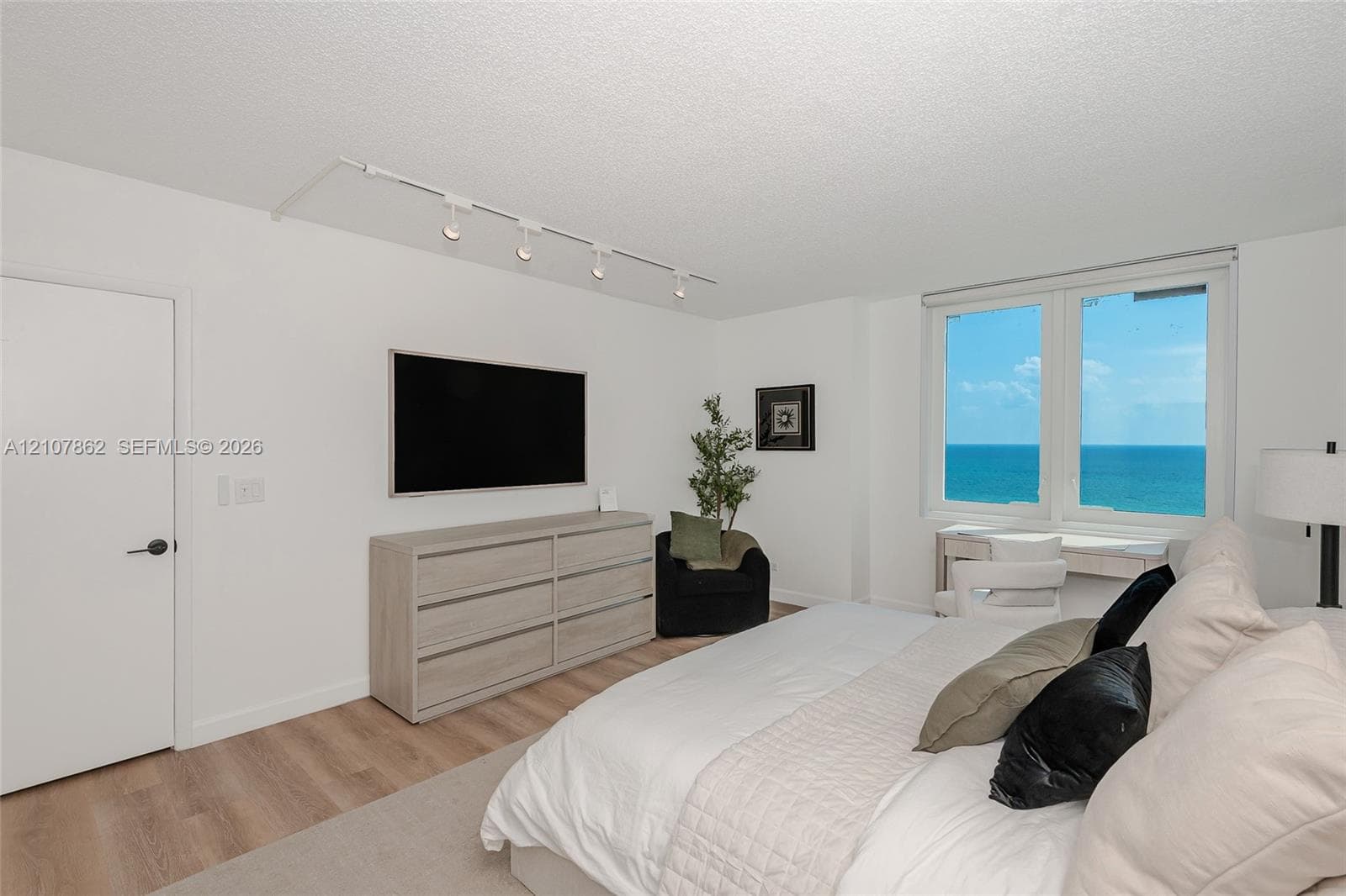 Interior space featuring wood-finish flooring, ceiling-mounted track lighting, and a large window with ocean scenery