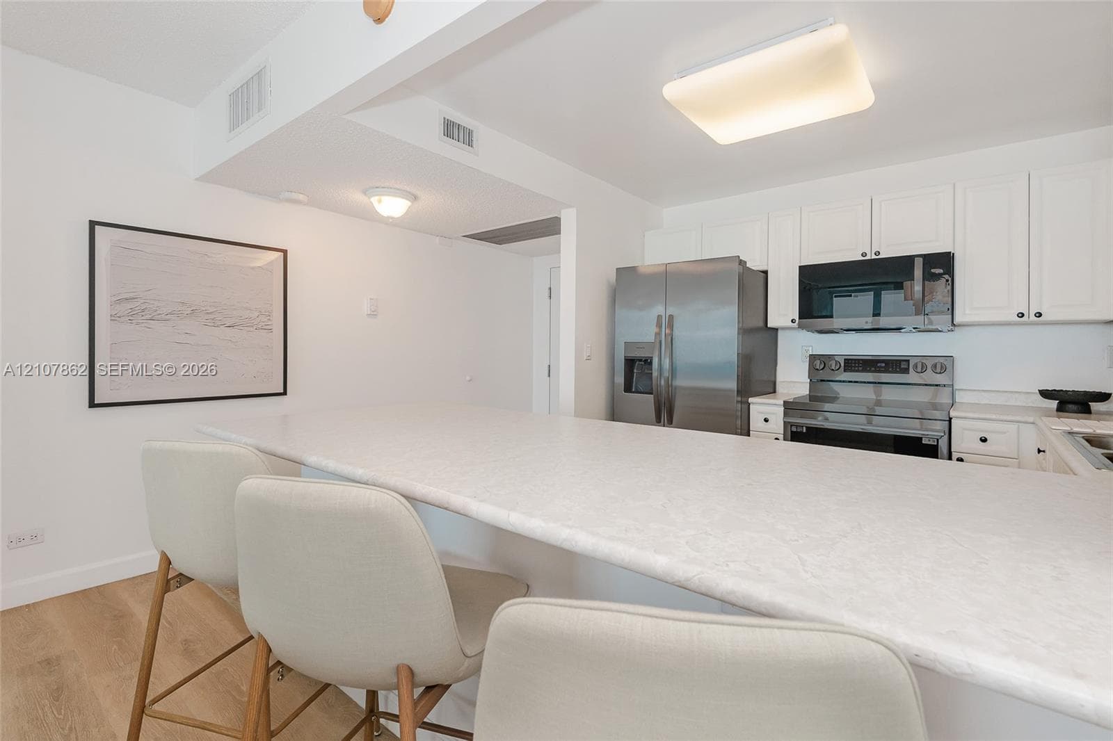 Kitchen featuring white cabinetry, solid-surface countertops with a breakfast bar, and stainless steel appliances, complemented by wood-finish flooring