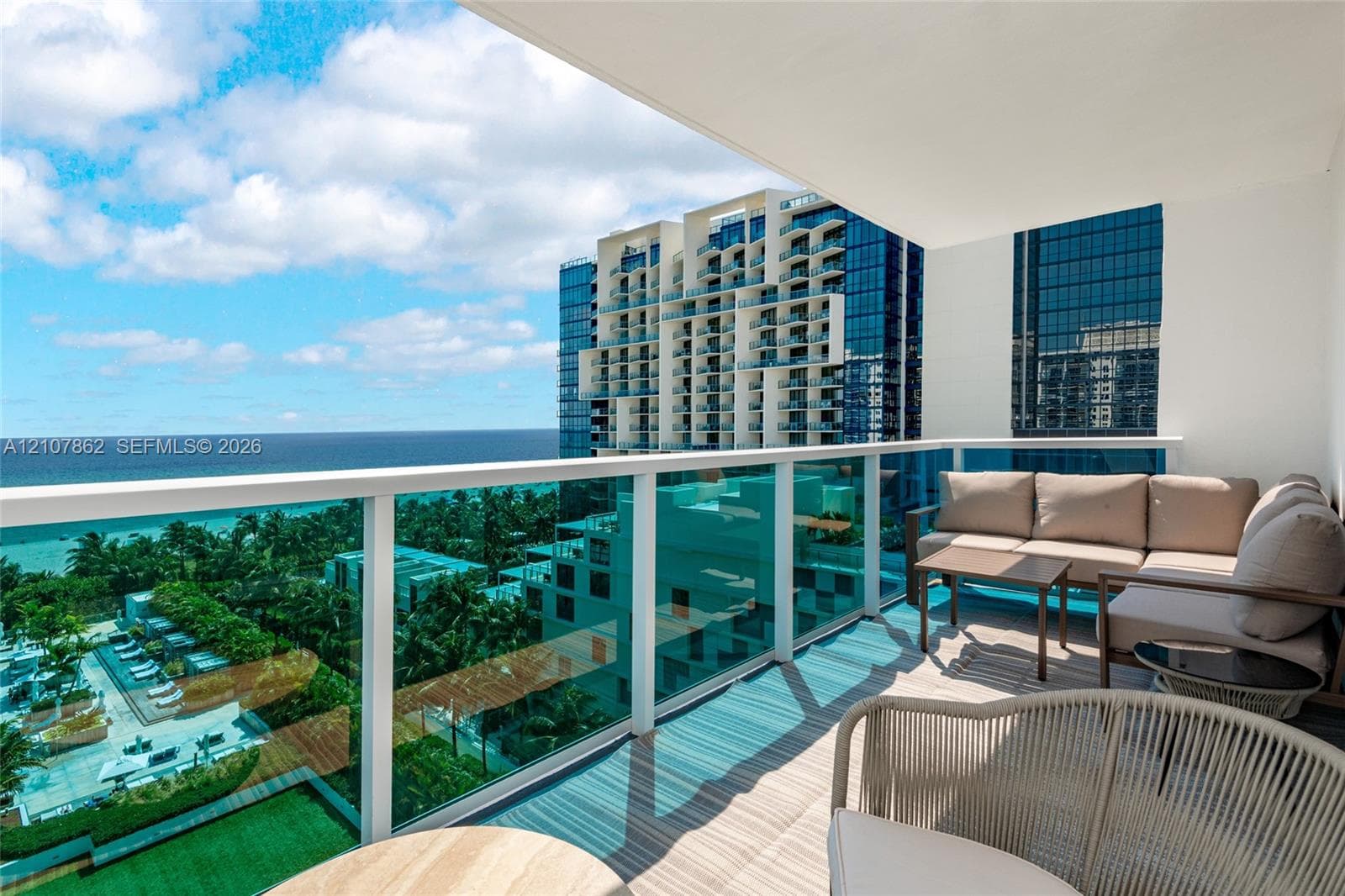Covered balcony featuring white structural framing, tempered glass railings, tile flooring, and a clear expanse of oceanic and metropolitan surroundings