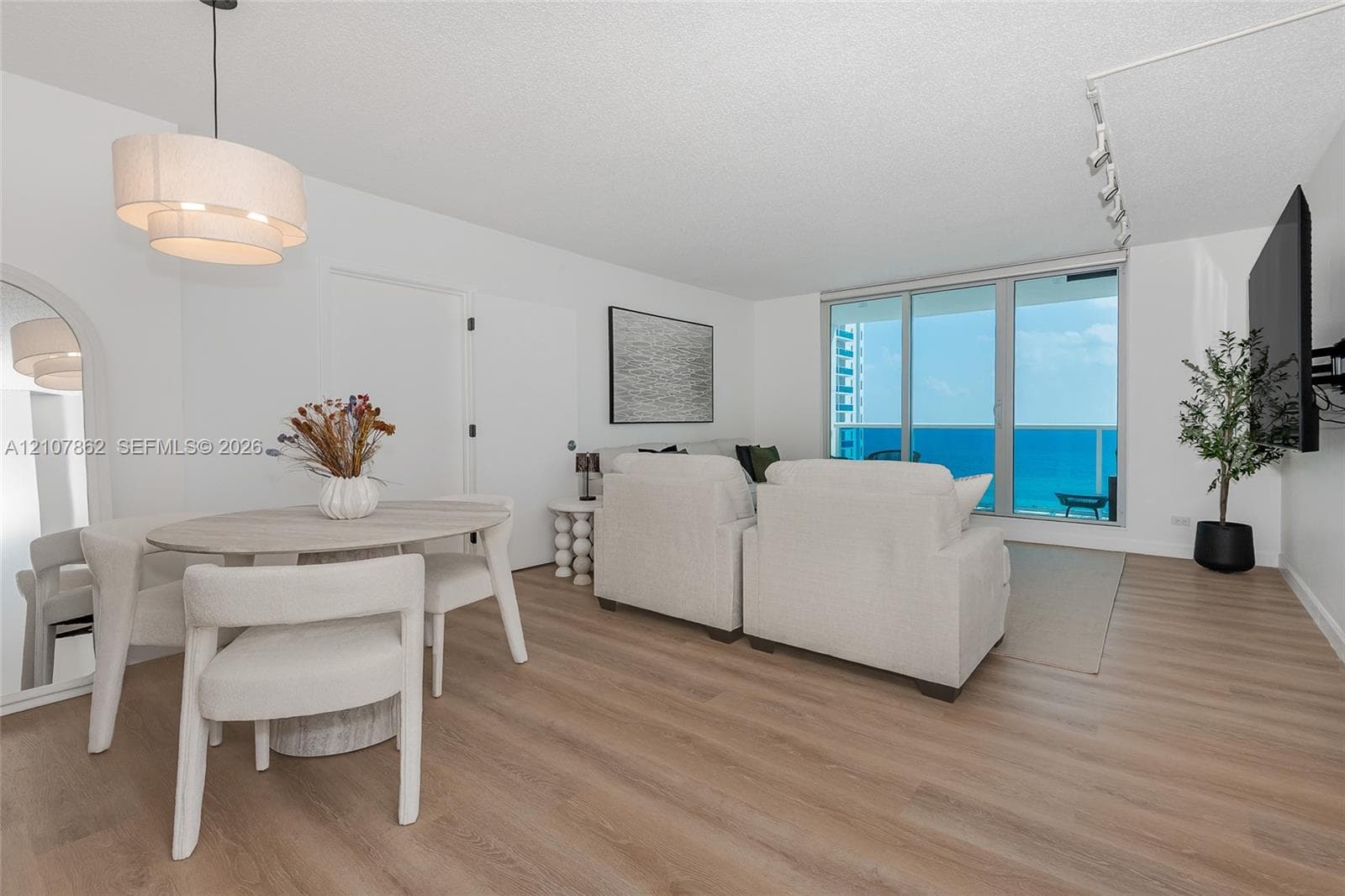Living space featuring wood-finish flooring, floor-to-ceiling sliding glass doors, arched wall mirror, layered drum pendant lighting, and adjustable track lighting
