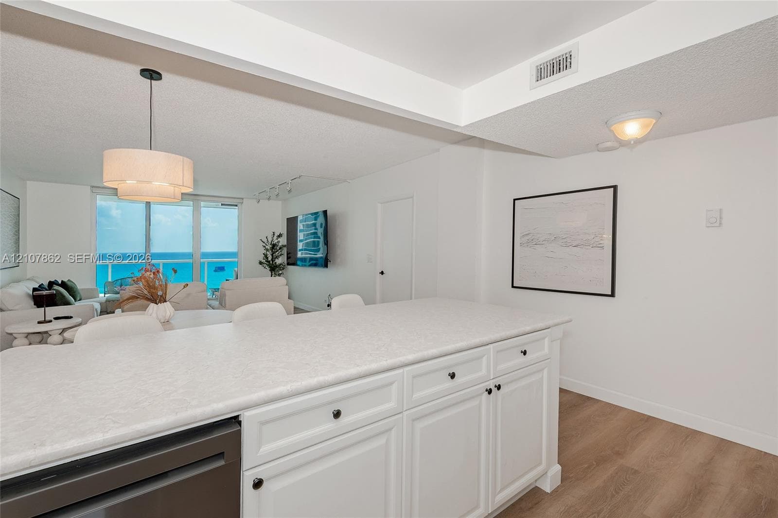 Kitchen island with white cabinetry and solid surface countertop, wood-finish flooring, and drum pendant lighting