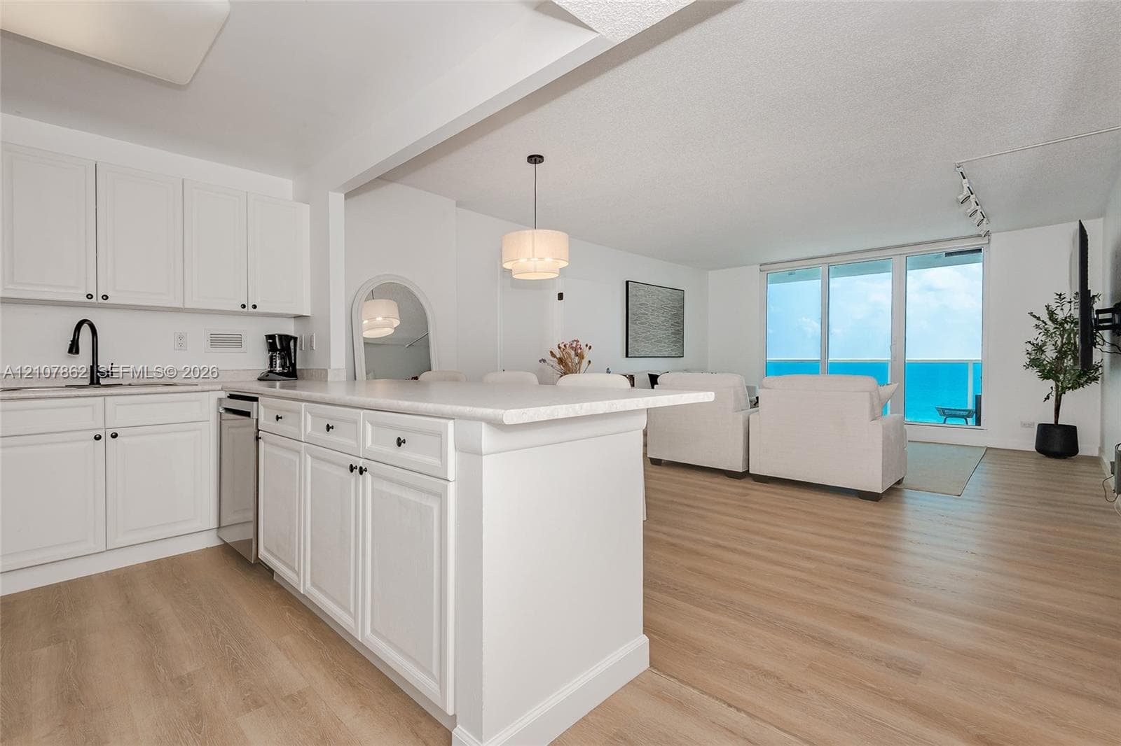 Kitchen featuring white cabinetry, solid-surface countertops, wood-finish flooring, and a matte black faucet, complemented by floor-to-ceiling sliding glass doors