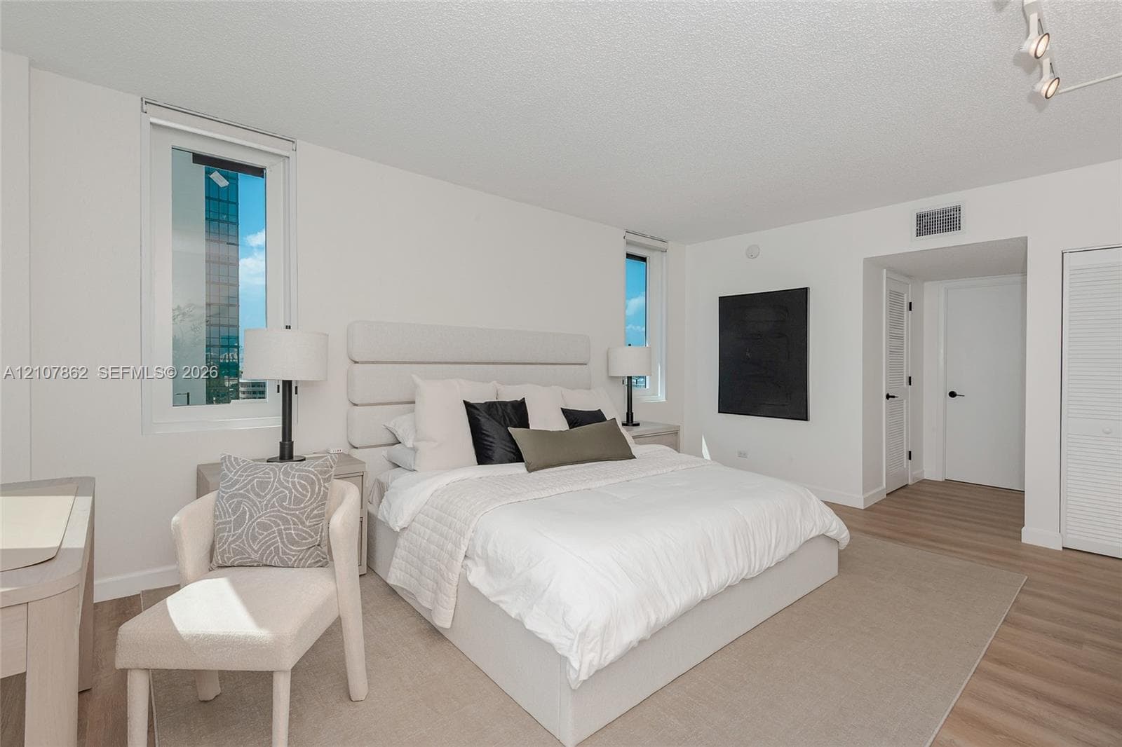 Spacious room featuring wood-finish flooring, dual windows, adjustable multi-head track lighting, and louvered closet doors