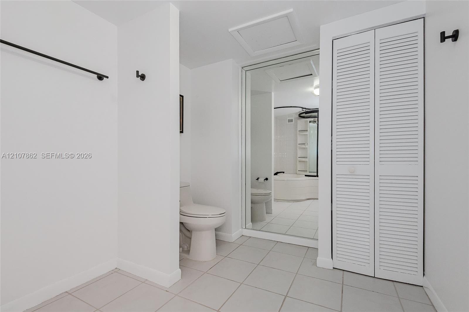Tile flooring, white louvered-door closet, full-length wall mirror, and dual-flush toilet