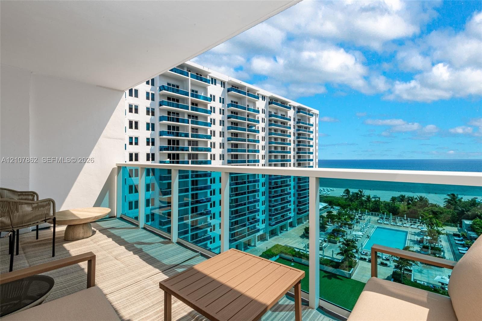 Private covered balcony featuring glass panel railings and a horizontal orientation overlooking the ocean and pool area