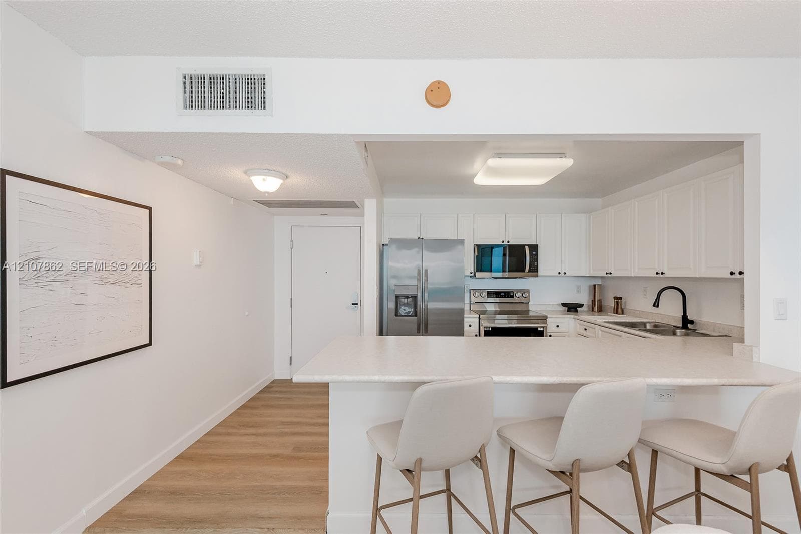 Kitchen featuring white cabinetry, stainless steel appliances, a peninsula with stone-finish countertop, and wood-finish flooring