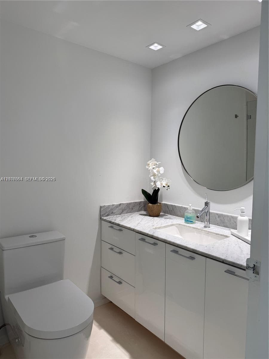 Modern vanity featuring high-gloss cabinetry, a stone-surfaced countertop with an integrated basin, a polished chrome single-handle faucet, and a large circular wall-mounted mirror