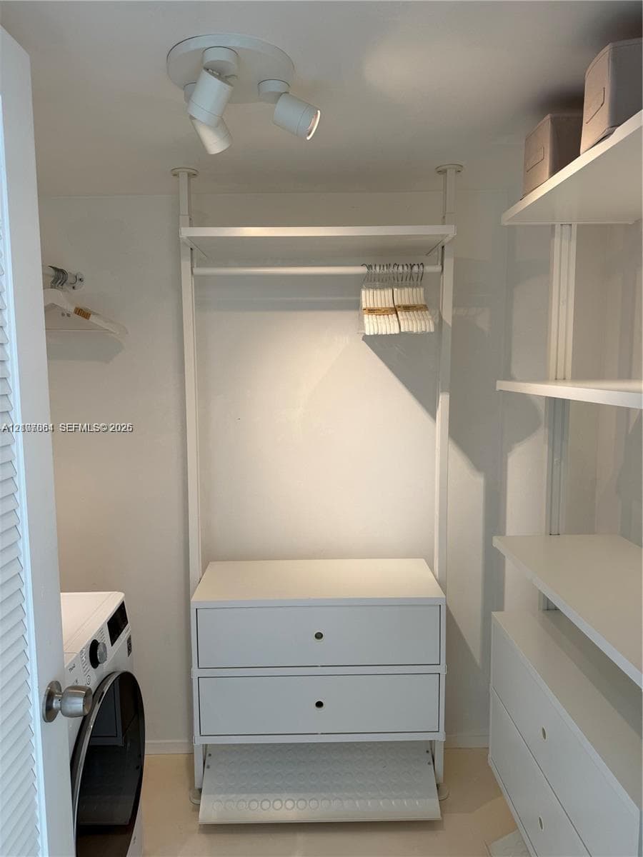 Built-in white storage system featuring integrated shelving, dual drawers, and a hanging rod, complemented by adjustable multi-directional track lighting