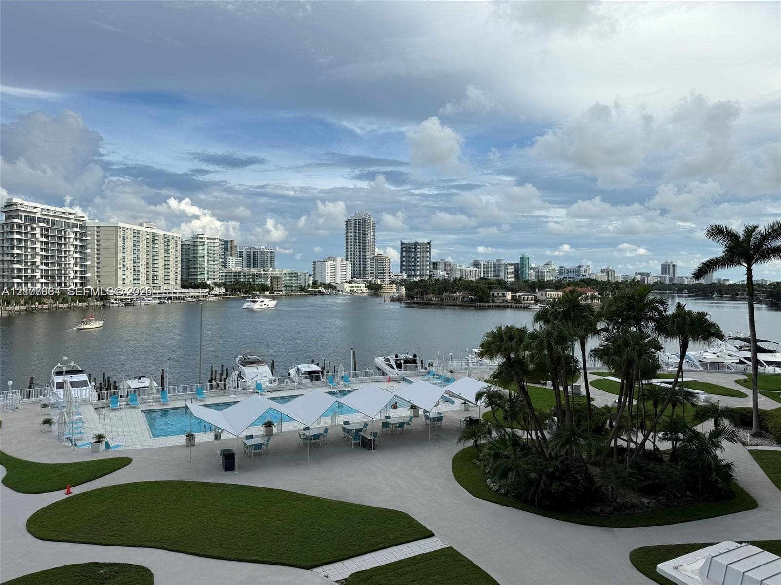 Waterfront property featuring a swimming pool, paved sundeck with tensioned shade structures, landscaped grounds, and boat slips
