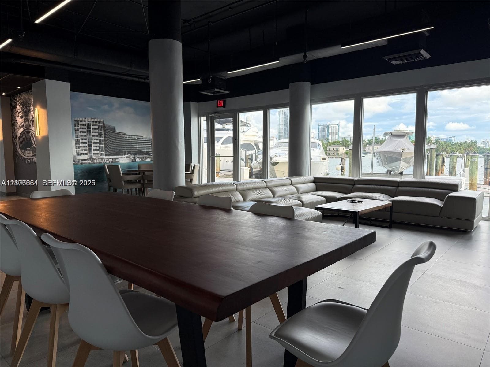 Open-concept interior featuring industrial-style exposed ceiling, structural cylindrical columns, expansive floor-to-ceiling windows, and large-format tile flooring