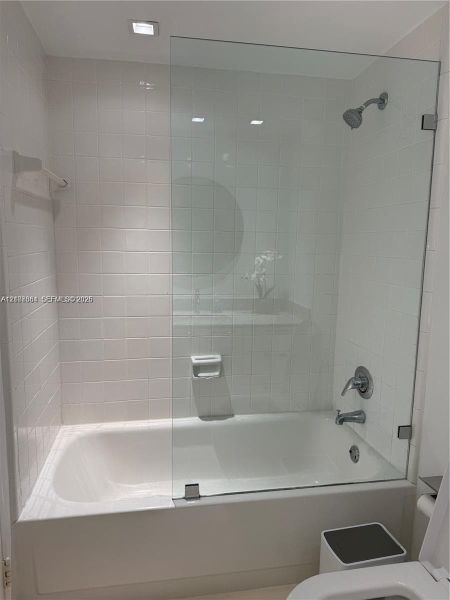 Bathtub enclosure featuring white ceramic wall tile, a frameless glass panel, polished chrome hardware, and a built-in recessed soap dish
