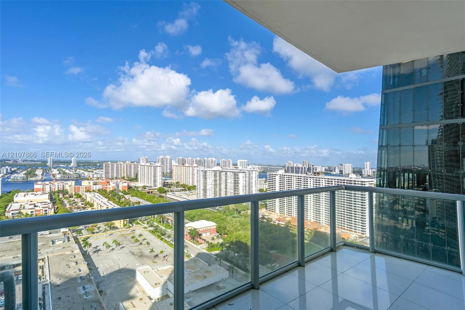 Private balcony featuring glass panel railings, tiled flooring, and high-rise urban surroundings