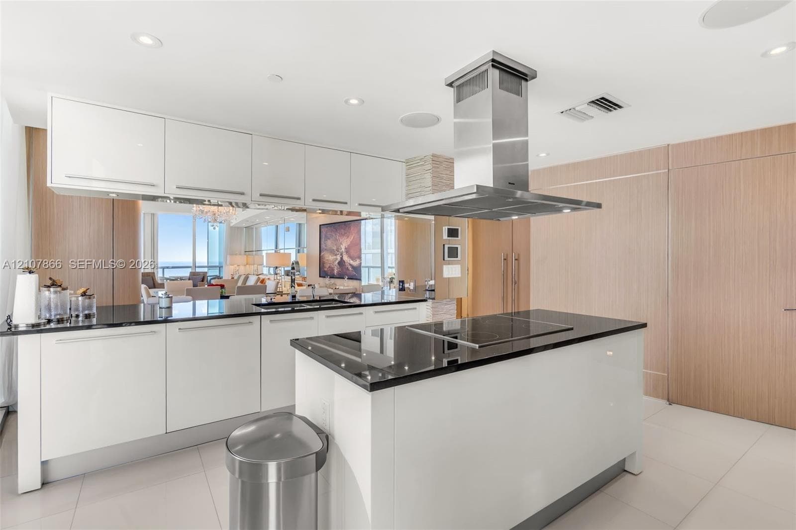 Modern kitchen featuring white flat-panel cabinetry, dark stone countertops, stainless steel island-mounted range hood, built-in cooktop, and wood-finish paneling