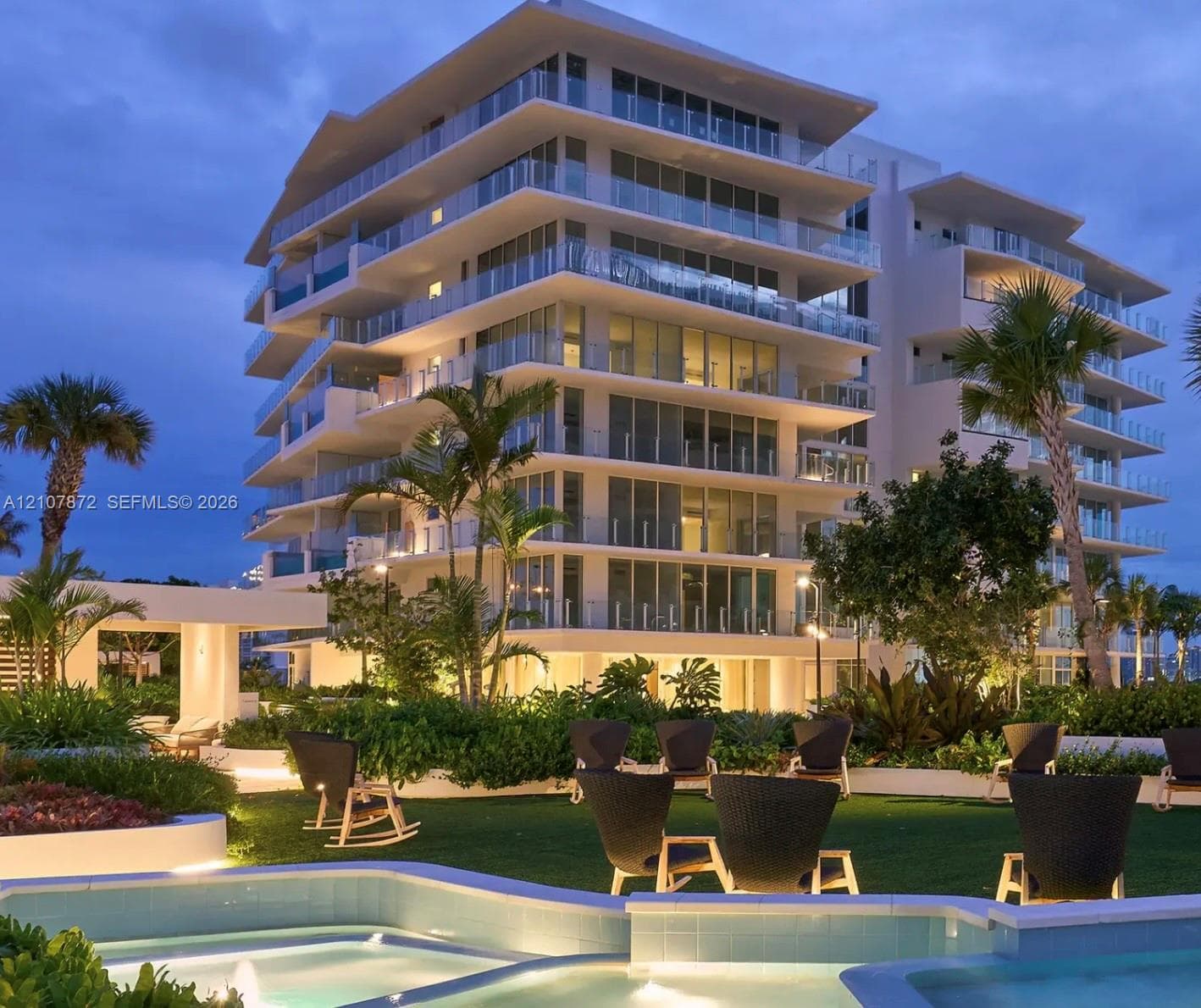 Mid-rise building exterior featuring tiered balconies with glass railings, an outdoor water feature with stone coping, and manicured landscaping