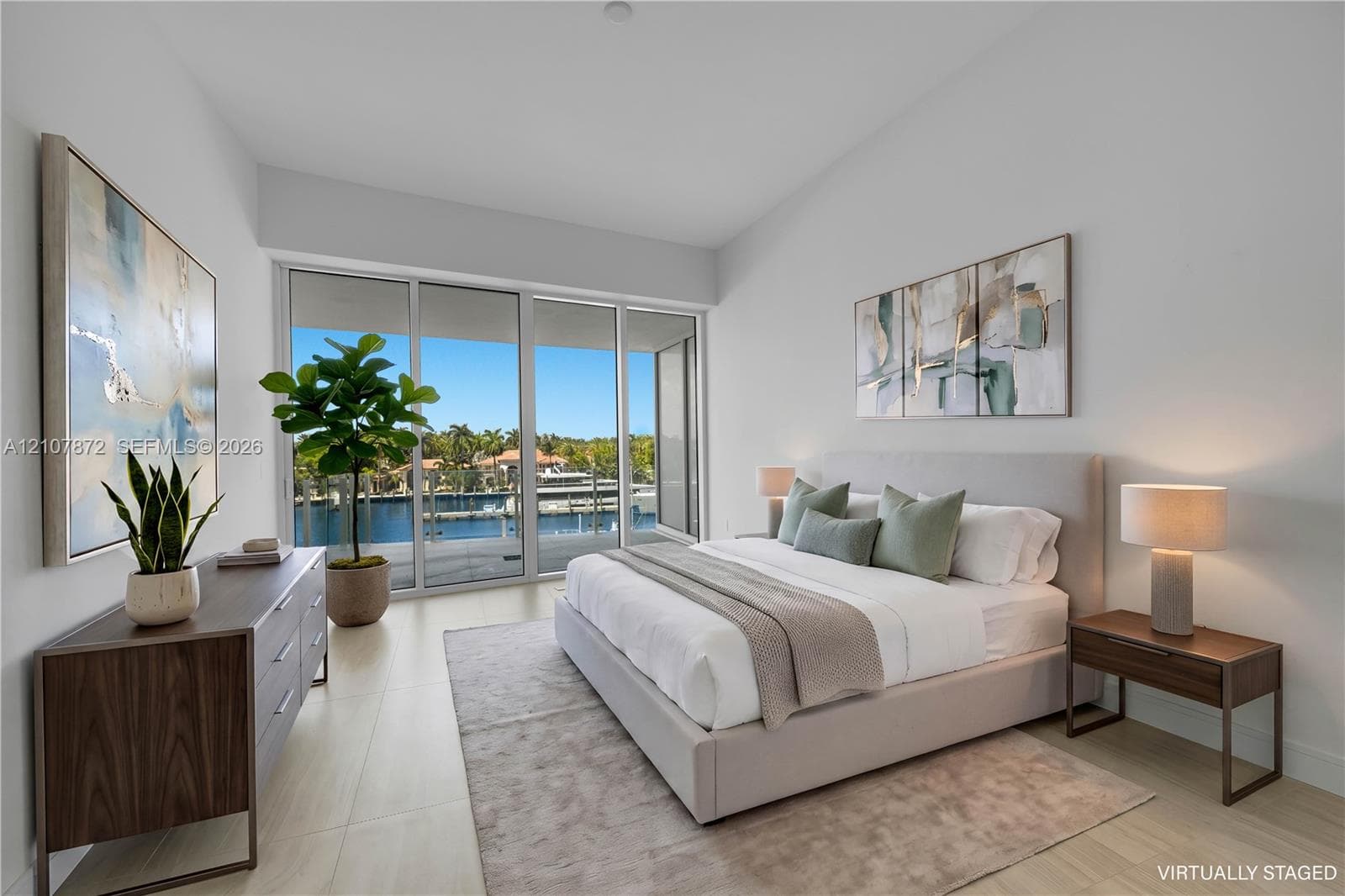 Floor-to-ceiling sliding glass doors, neutral tile flooring, and direct access to an outdoor balcony featuring a waterfront and marina setting