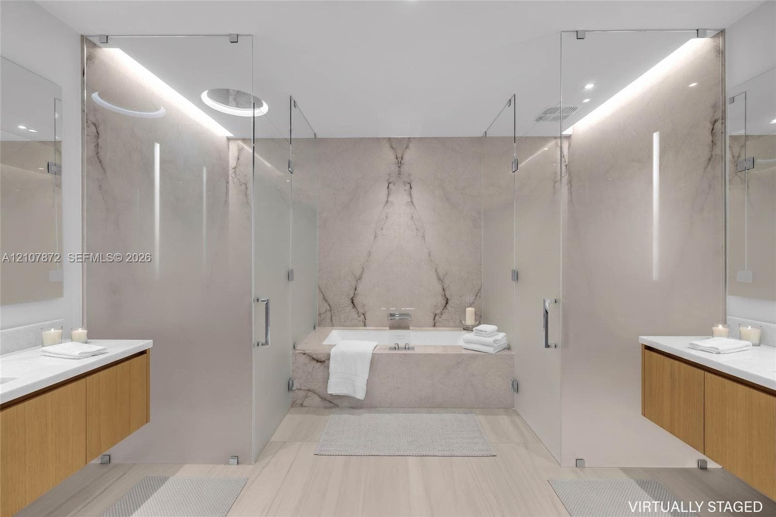 Dual floating wood-finish vanities with rectangular integrated sinks, stone-clad drop-in bathtub with wall-mounted faucet, full-height stone backsplash, and frameless glass-enclosed shower stalls with recessed overhead lighting