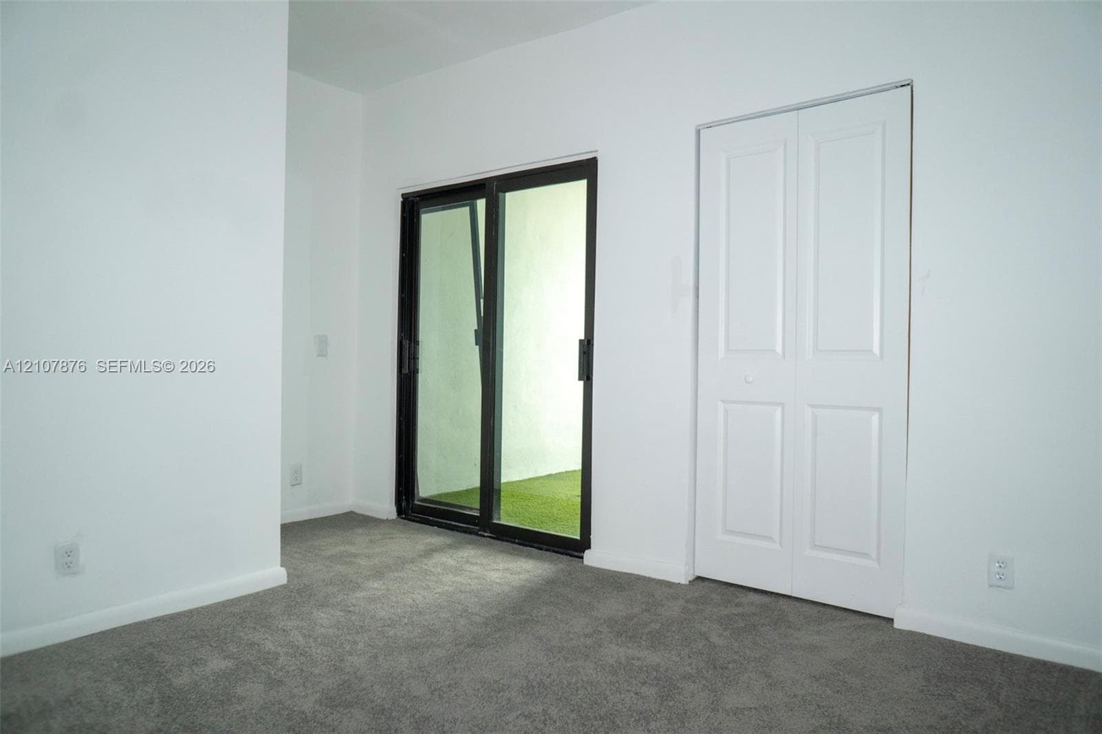 Interior space featuring neutral carpeting, a two-panel sliding closet door, and a sliding glass door with a dark frame