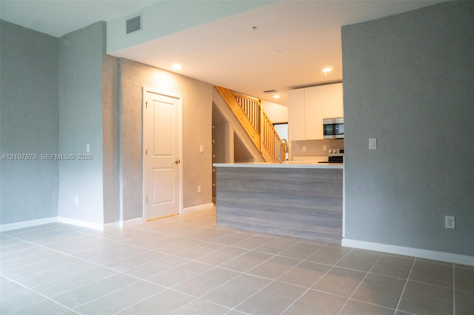 Neutral tile flooring, kitchen island with wood-finish paneling, white flat-panel cabinetry, and staircase with wooden railings