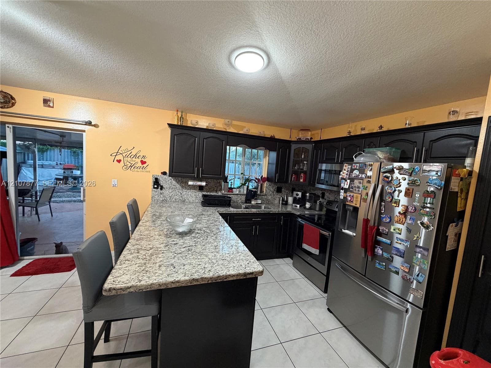 Kitchen featuring dark cabinetry, stone-surface countertops with a breakfast bar, stainless steel appliances, and tile flooring