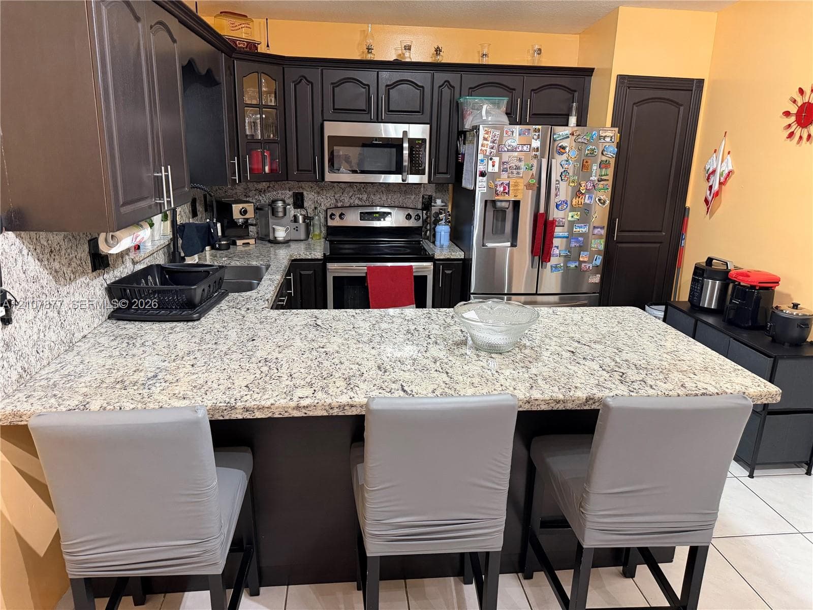 Kitchen featuring dark cabinetry, expansive stone countertops, stainless steel appliances, and tiled flooring