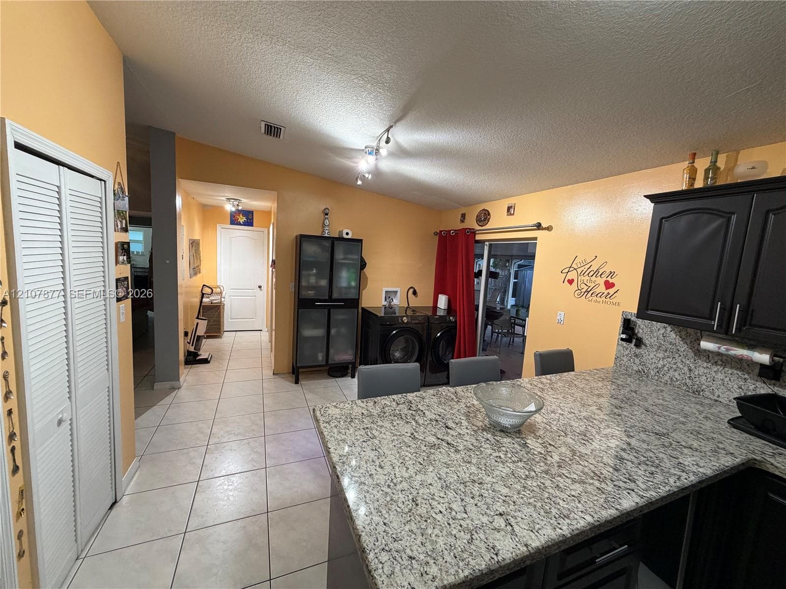 Kitchen featuring stone-finish countertops, dark cabinetry, ceramic tile flooring, and integrated laundry area with dual folding doors