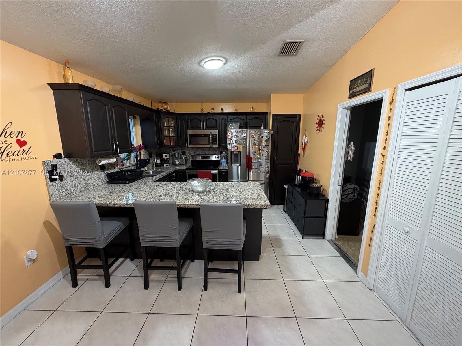 Kitchen featuring dark cabinetry, stone-surface countertops, tile flooring, stainless steel appliances, and a breakfast bar
