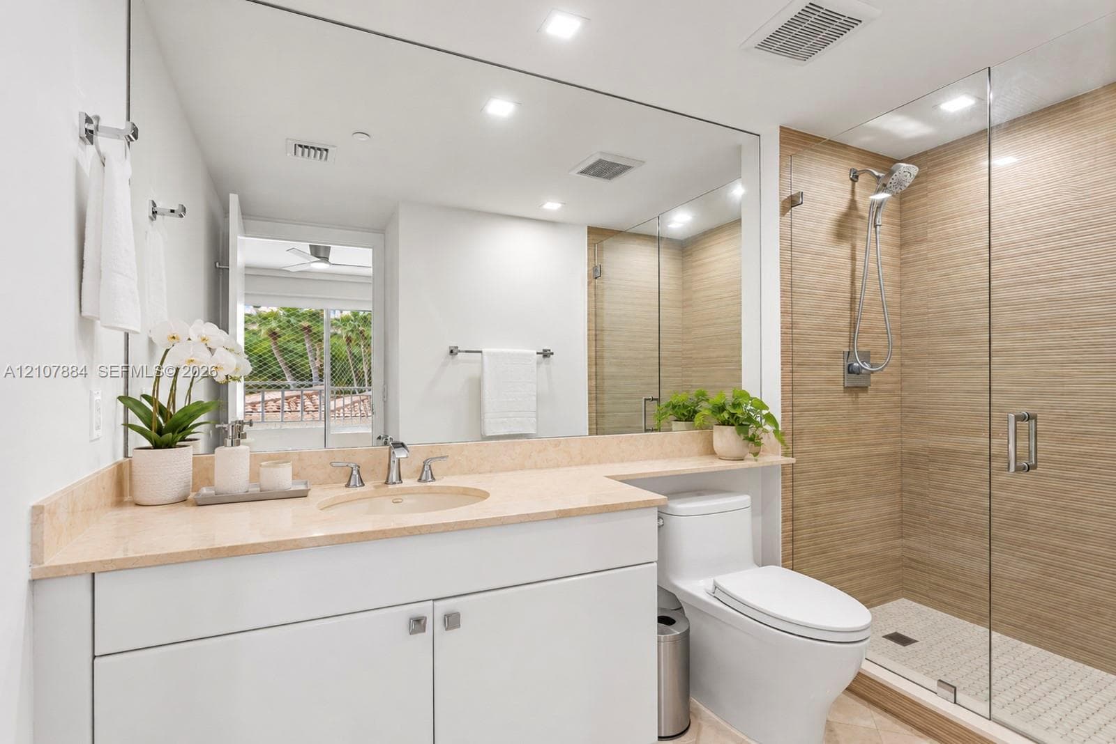 Bathroom featuring a white vanity with a neutral stone countertop, full-width wall mirror, walk-in glass-enclosed shower with horizontal tile surround, and recessed lighting