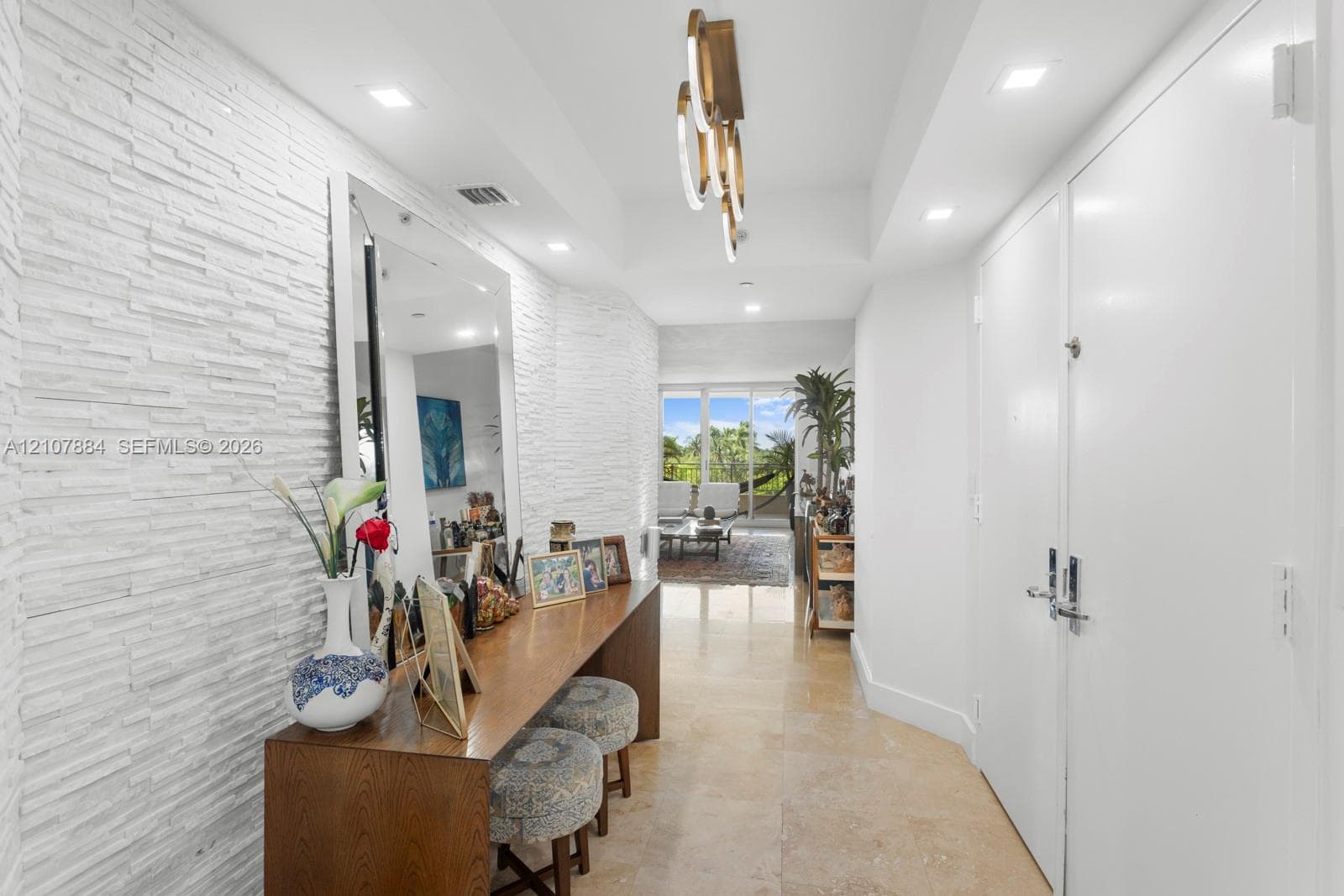 Entryway featuring white stacked-stone wall cladding, polished stone flooring, recessed ceiling lighting, and a contemporary multi-tiered metal chandelier